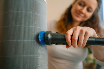 Woman cleaning a dirty air purifier filter with a vacuum brush, removing dust to improve indoor air quality and prevent allergies in a modern home routine