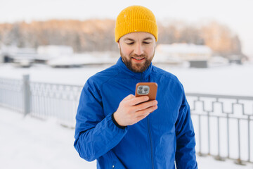 Obraz premium Man checking smartphone for navigation or fitness tracking while exercising outdoors in snowy winter park