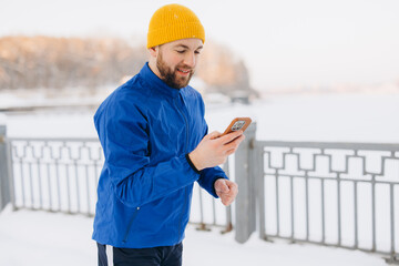 Male runner checking workout data on smartphone during a cold winter outdoor training session in...