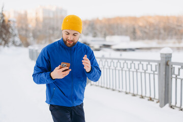 Man walking outdoors in winter using smartphone, connecting with technology during a fitness activity