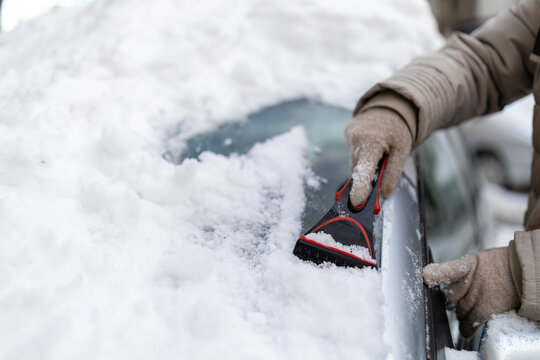 Person scraping deep snow from car windshield