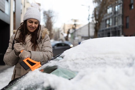 Woman scraping snow from car windshield on winter day