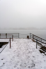 Fototapeta premium Snow covers a pier near a lake with fog surrounding the area during winter in a quiet, remote location