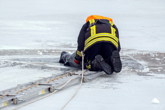 Firefighter helps person stranded on ice at frozen lake during emergency rescue operation in winter weather conditions