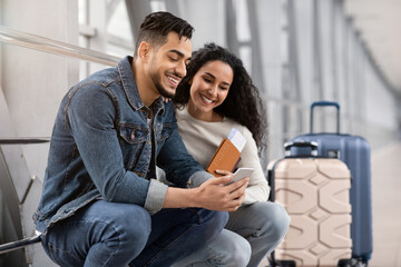 Obraz premium Waiting For Flight. Young Arab Spouses Using Smartphone In Airport Terminal, Middle Eastern Couple Browsing Internet On Mobile Phone Or Booking Hotel Online Before Flight Boarding, Closeup Shot