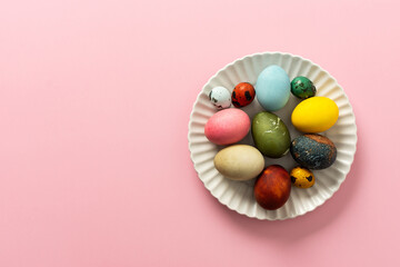A collection of vibrant Easter eggs in various colors is artfully arranged on a white plate, set against a soft pink background, capturing the essence of the holiday's decorations