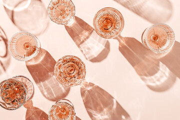 Minimal composition Top view glasses of rose wine or champagne on pink background, artistic shadows and sun flare. Aesthetic still life crystal wineglass, sparkling drinks for summer party, copyspace