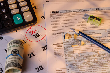 Close up of a hundred dollar bill on IRS Form 1040 in color and a calendar with a red circle on the 15th in bright morning sunlight.