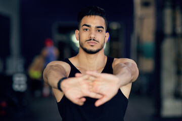 Fototapeta premium Portrait Of Sporty Young Arab Man Stretching Arms At Camera, Confident Middle Eastern Male Athlete Warming Up Before Training At Gym, Ready For Fitness Workout, Closeup Shot, Selective Focus