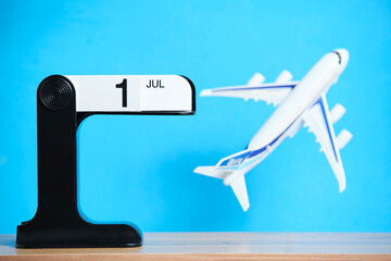 Flip calendar with date July 1 and flying plane on blue background symbolizes travel plans and new beginnings.