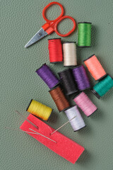 Colorful sewing threads and scissors on green background. Top view.