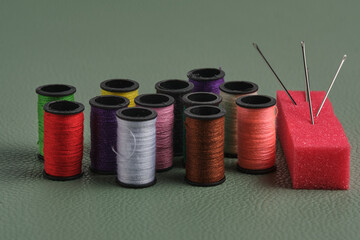 Spools of thread and needles on green background, sewing concept.