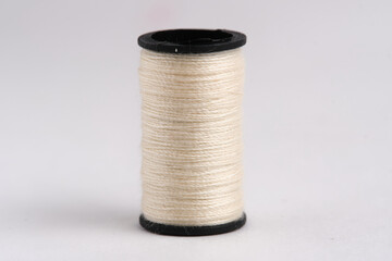 Spool of beige thread on white background. Closeup.