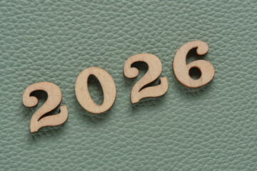 Wooden numbers 2026 on green leather texture background, business concept.