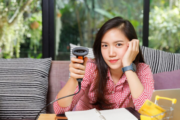 Young Asian female online seller holding barcode scanner gun while working on e-commerce business at home.