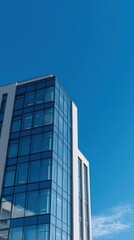 Obraz premium Modern Glass Building with Vertically Rising Structure Against Clear Blue Sky