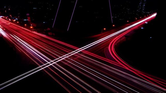Dynamic long exposure photograph of red and white light trails from vehicles on a dark highway at night, creating an abstract pattern of movement.