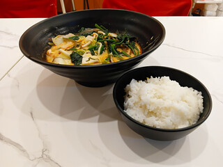 Spicy mala soup served in a black bowl, filled with vegetables and herbs, rich chili broth, hot flavor, Asian comfort food style. with rice