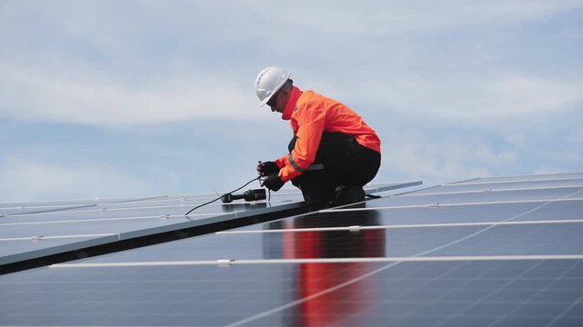 Technician installing solar panels on factory roof for green energy. A skilled technician in safety gear is working on a solar panel installation on rooftop. clean energy renewable power technology.