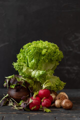 Still life with fresh lettuce, potatoes, and radishes arranged on a dark wooden background. Rustic vegetable composition with natural textures