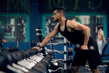 Naklejka premium Sport Training. Confident Muscular Arab Guy Lifting Heavy Barbell With One Hand At Gym, Motivated Middle Eastern Male Athlete Enjoying Bodybuilding Exercises, Working On Biceps Muscles At Sport Club