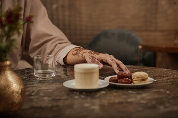 Henna hand beside Arabic coffee and date cookies in warm modern cafe