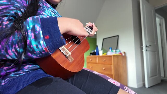 A young child strums a ukulele with curiosity and joy, symbolizing early musical learning, creativity, and the desire to explore music through a simple instrument.