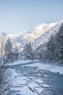 Wild alpine river flowing through a frozen winter valley with snow-covered mountains. The Lech River in the Lechtal Nature Park near Holzgau, Tyrol, Austria, under cold and clear winter conditions.