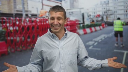 Man smiling and pointing on a construction street with urban barriers and worker in view.