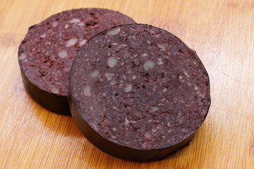 Two slices of raw black pudding on wooden cutting board