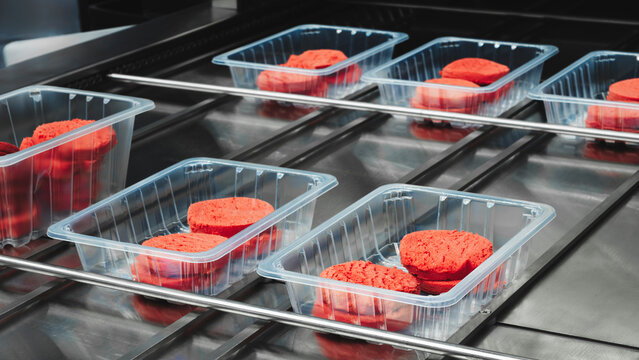 Clear, open plastic boxes containing red cookies are being processed. Several trays are on a conveyor belt, ready for further packaging and transportation.