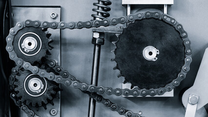 A chain with two gears on it. The chain is black and silver. The chain is connected to a machine
