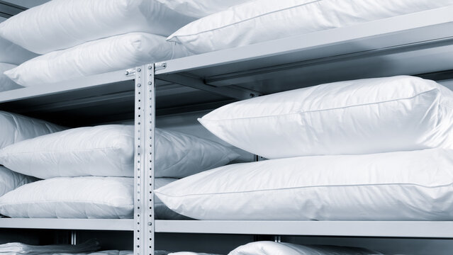 A white shelf with many white pillows stacked on top of each other. pillows are all the same size and color, and they are neatly arranged on the shelf. Concept of order and