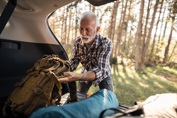 Senior man packing backpack from car trunk for hiking adventure © Jelena