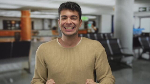 Man flashes broad face to cheer passengers in airport where young hispanic traveler stands by terminal during waiting male anticipation.
