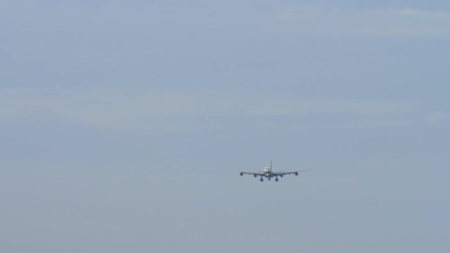 A huge four-engine aircraft with an unrecognizable livery approaching landing, front view long shot. Airplane in blue sky background. Travel concept