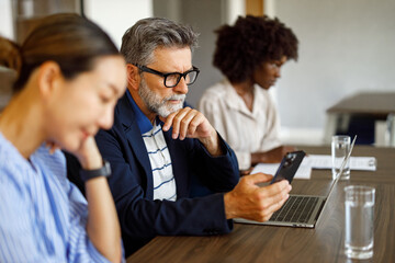 Serious male lawyer reading messages on mobile phone while working with female colleagues in board room