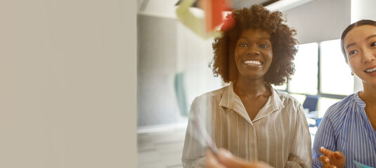Smiling female professionals discussing strategies in office during collaborative meeting seen through glass wall