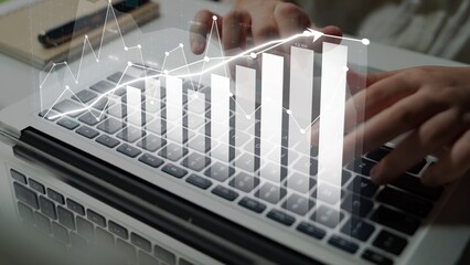 A close-up view of hands typing on a modern laptop keyboard, showcasing a digital graph overlay that highlights growth trends and data analysis in a professional setting. Copula