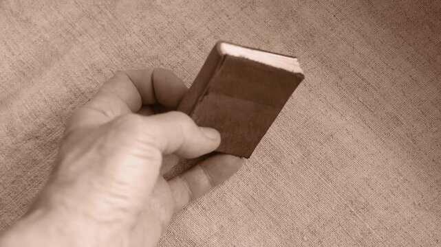 Miniature leather-bound book on a rough hemp tablecloth. Handmade book for personal notes in a woman's hand. DIY mini book. Sepia effect.