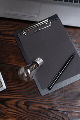 Light bulb lying on a black notebook with a pen. Concept of electricity, energy, ideas, and creative thinking in a minimalistic workspace.