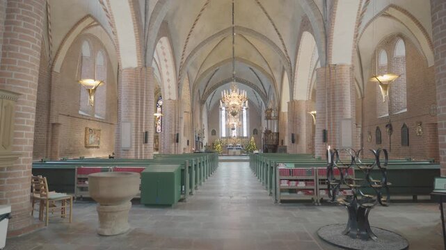 A tranquil view of a church interior featuring high arched ceilings, elegant lighting, and rows of seating. The architectural details create a peaceful atmosphere, ideal for reflection and worship.