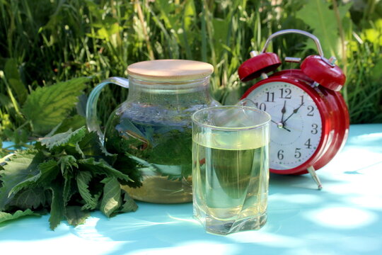 A decoction of nettle leaves in a teapot stands on a wooden table.	