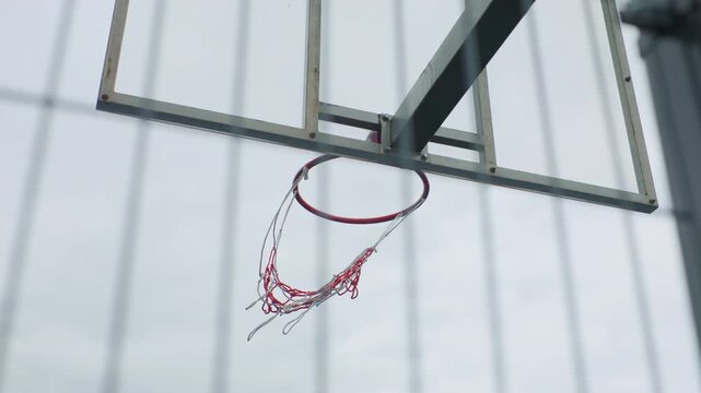 closeup basketball hoop with rippling net, ball absent, net twisting downward after clean swish, metallic rim gleaming, backboard mount visible, brisk overcast light, high shutter detail, outdoor