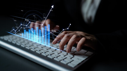 A business professional is typing on a keyboard with digital graphs and charts displayed,...