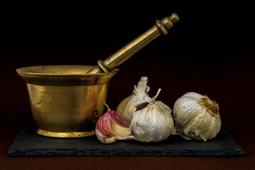 Brass mortar and pestle with whole garlic bulbs on dark slate background