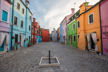 Colorful houses of Burano island near Venice showcasing vibrant pastel facades, narrow streets, and traditional Italian architecture in a quiet residential square under soft daylight sky
