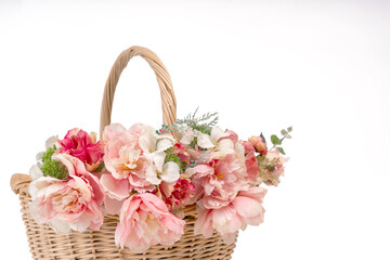 Close-up view of a wicker basket filled with delicate pastel pink peonies and roses arranged in a soft romantic composition. The detailed petals and natural textures create an elegant spring atmospher