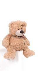 Obraz premium Soft brown teddy bear sitting on a white pedestal against a clean white background. The fluffy texture and warm neutral tones create a cozy, comforting, and nostalgic childhood atmosphere
