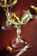A martini in a crystal glass, bathed in golden hour lighting, with olives resting on a cocktail...